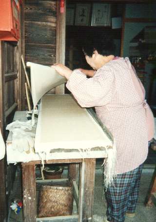 Mrs. Fukunishi lifts a sheet of paper onto a dowel